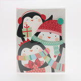 X-mas Melody Card(XC265) featuring three cheerful penguins in festive hats and scarves with a Christmas gift.