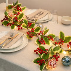 Christmas Holly Berry Garland with LED Lights – Festive Table Decoration on a dining table with dishes and lights.